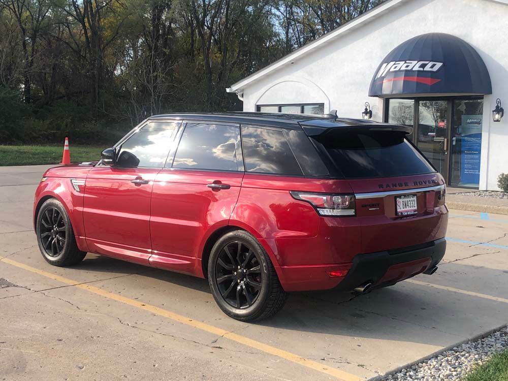 A red range rover sport is parked in a parking lot in front of a building.