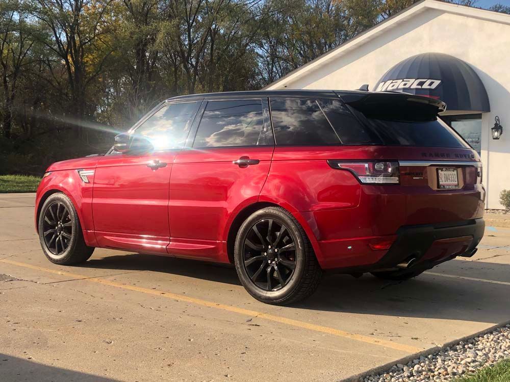 A red range rover sport is parked in a parking lot in front of a building.