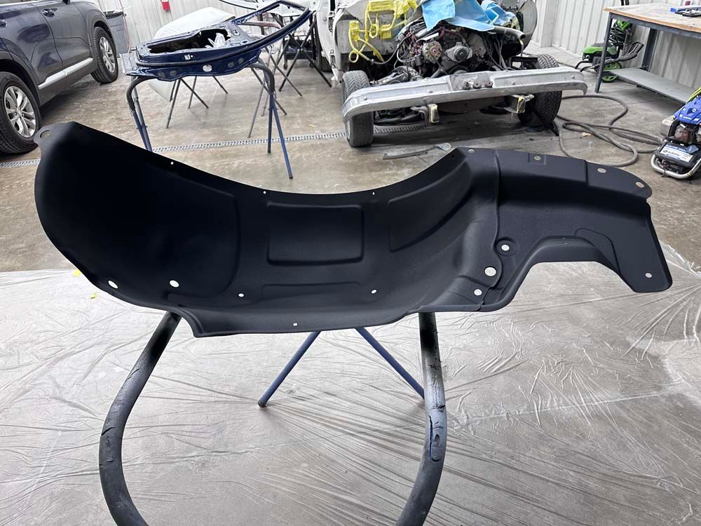 A black fender is sitting on a stand in front of a car.