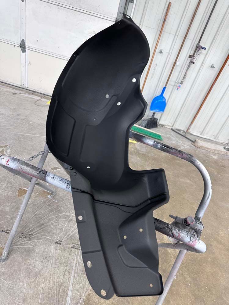 A black fender liner is sitting on top of a metal stand.