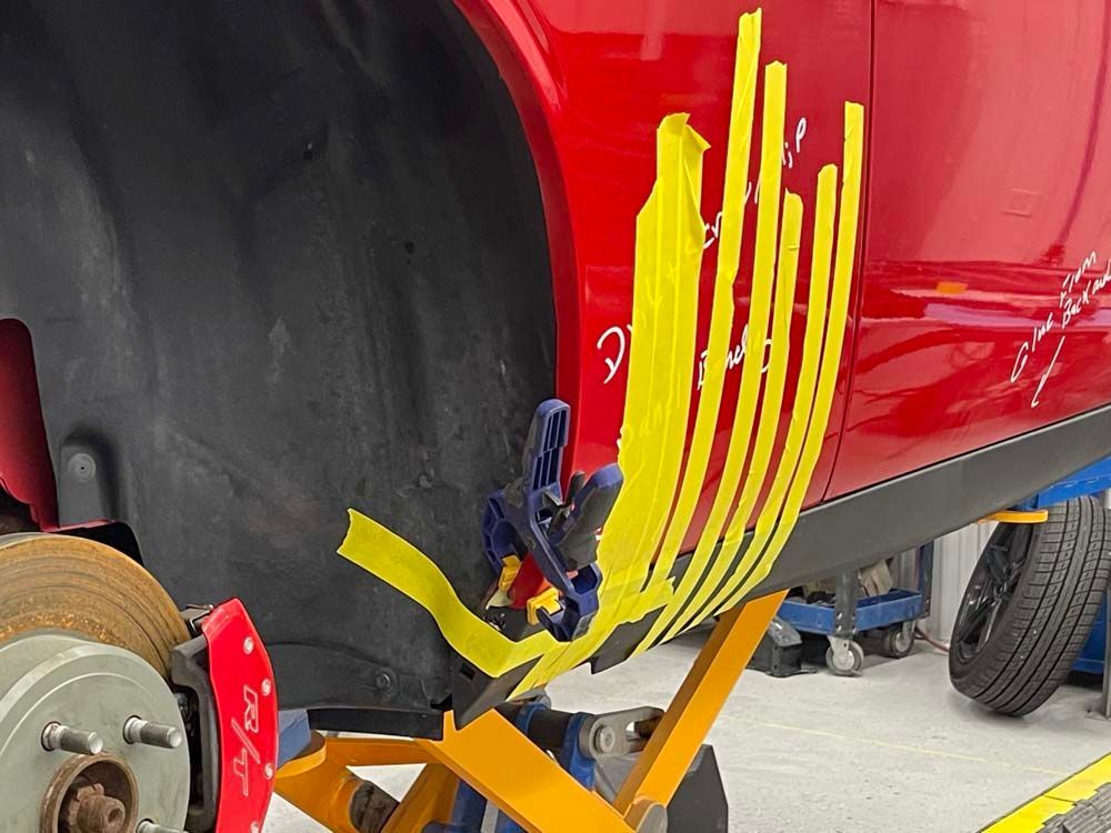 A red car with yellow tape on it is sitting on a lift.