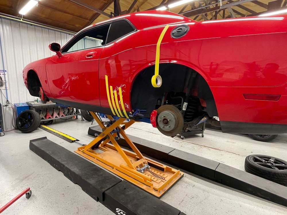 A red dodge challenger is sitting on a lift in a garage.