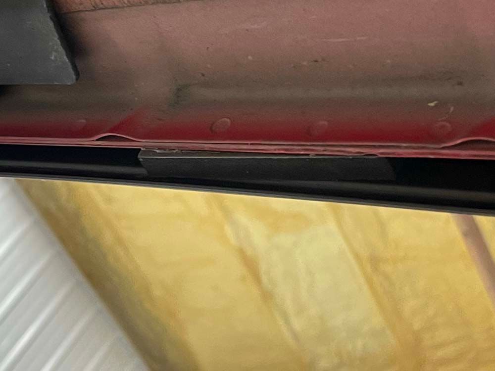 A red car is parked in a garage next to a wooden wall.