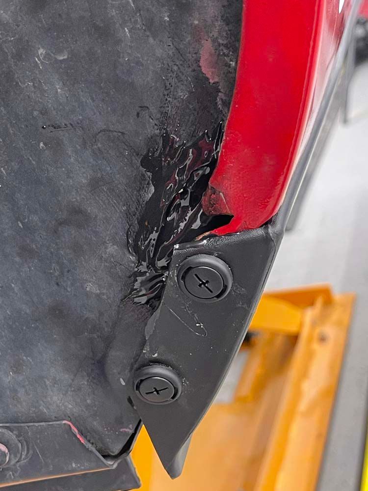 A close up of a red car fender with screws on it.