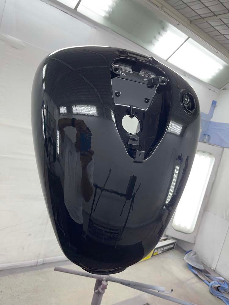 A black motorcycle tank is sitting on a stand in a paint booth.
