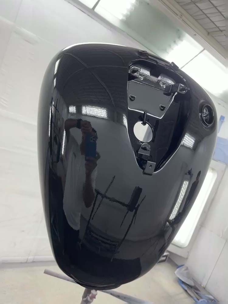 A black motorcycle tank is sitting on a stand in a paint booth.