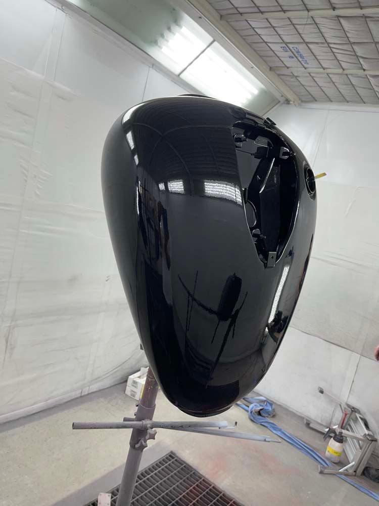 A black motorcycle tank is sitting on a stand in a paint booth.