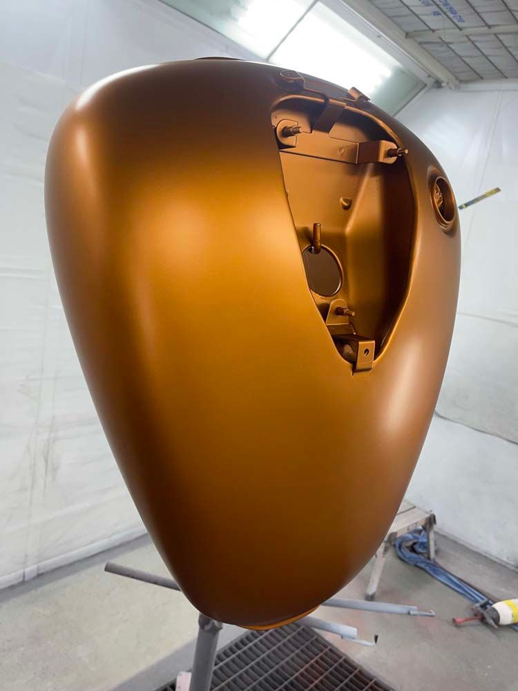 A motorcycle tank is sitting on a stand in a paint booth.