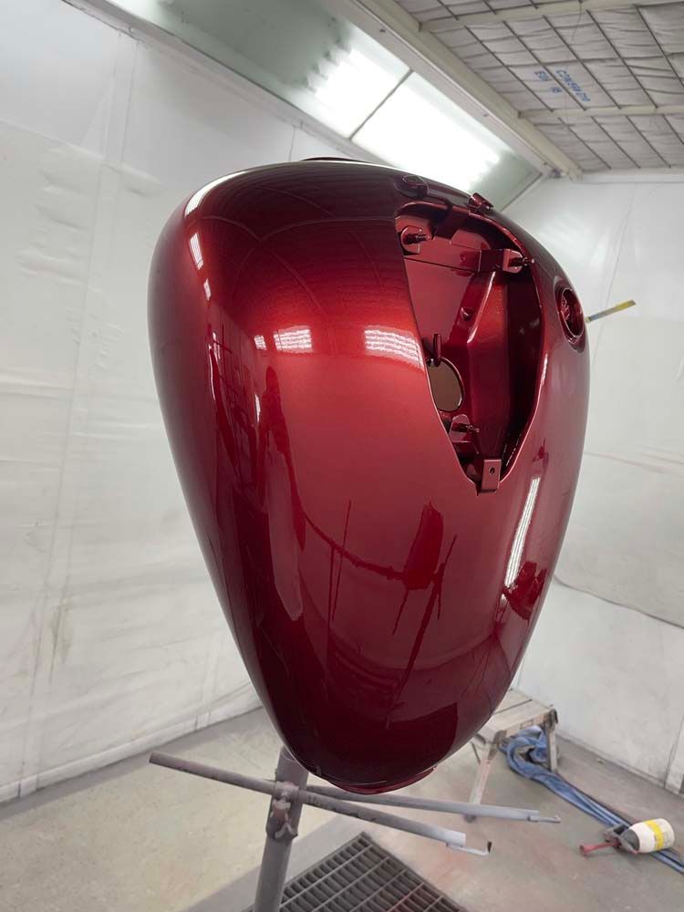 A red motorcycle tank is sitting on a stand in a paint booth.