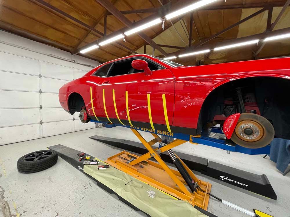 A red car is sitting on a lift in a garage.