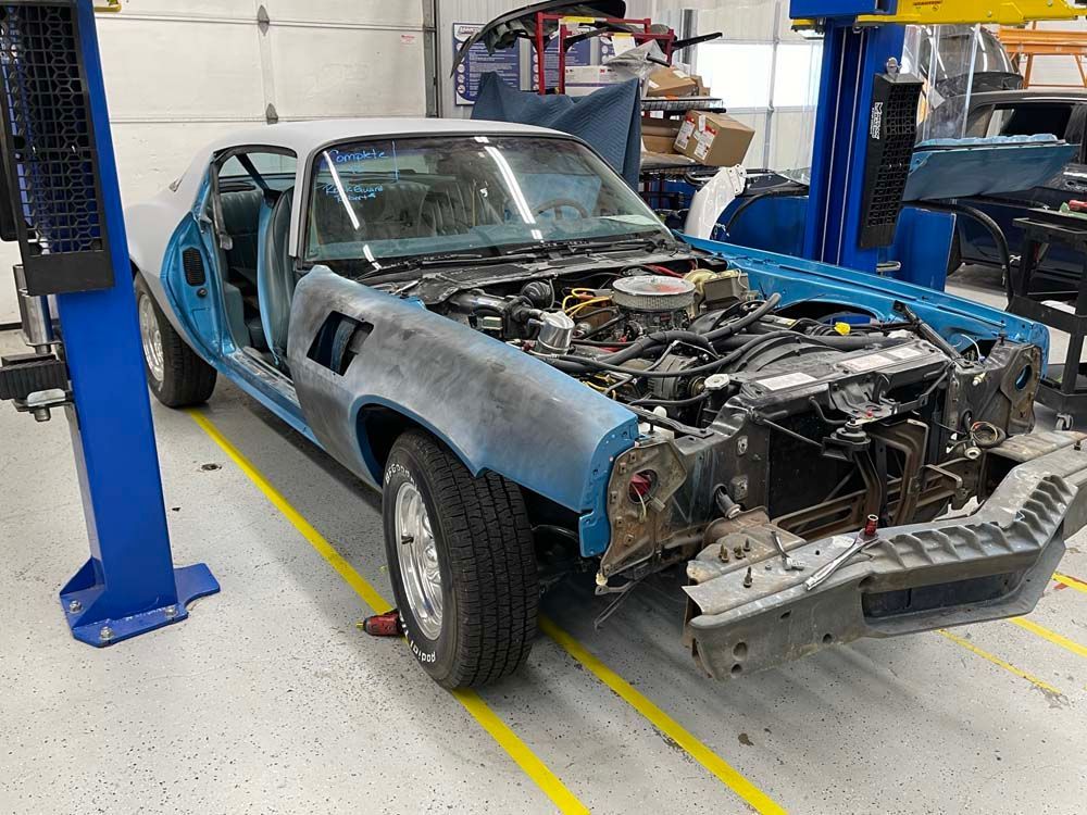 A blue car with the hood open is on a lift in a garage.