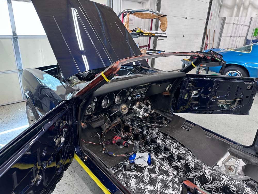 A black car with the hood up is being worked on in a garage.