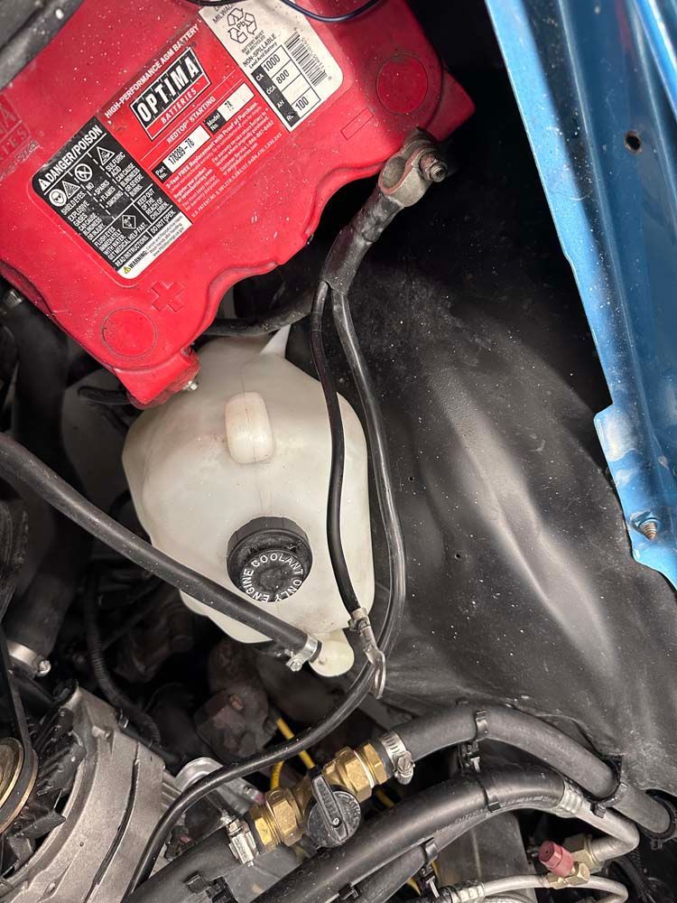 A red battery is sitting under the hood of a blue car.