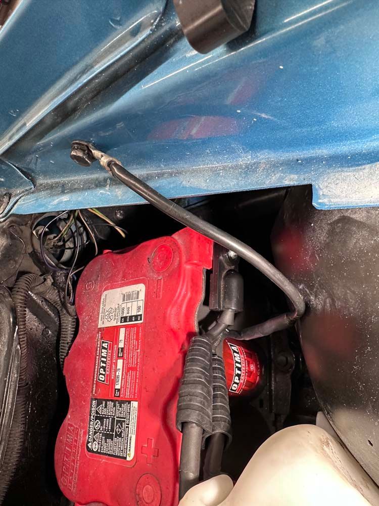 A red battery is sitting under the hood of a blue car.