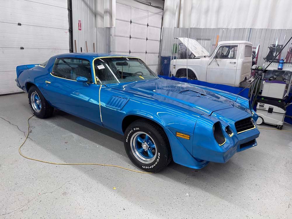 A blue car is parked in a garage next to a truck.