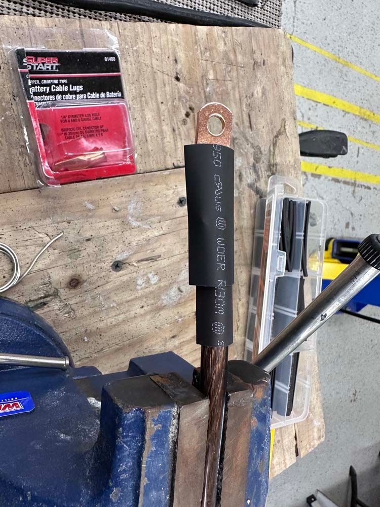 A piece of wire is being held in a vise on a wooden table.