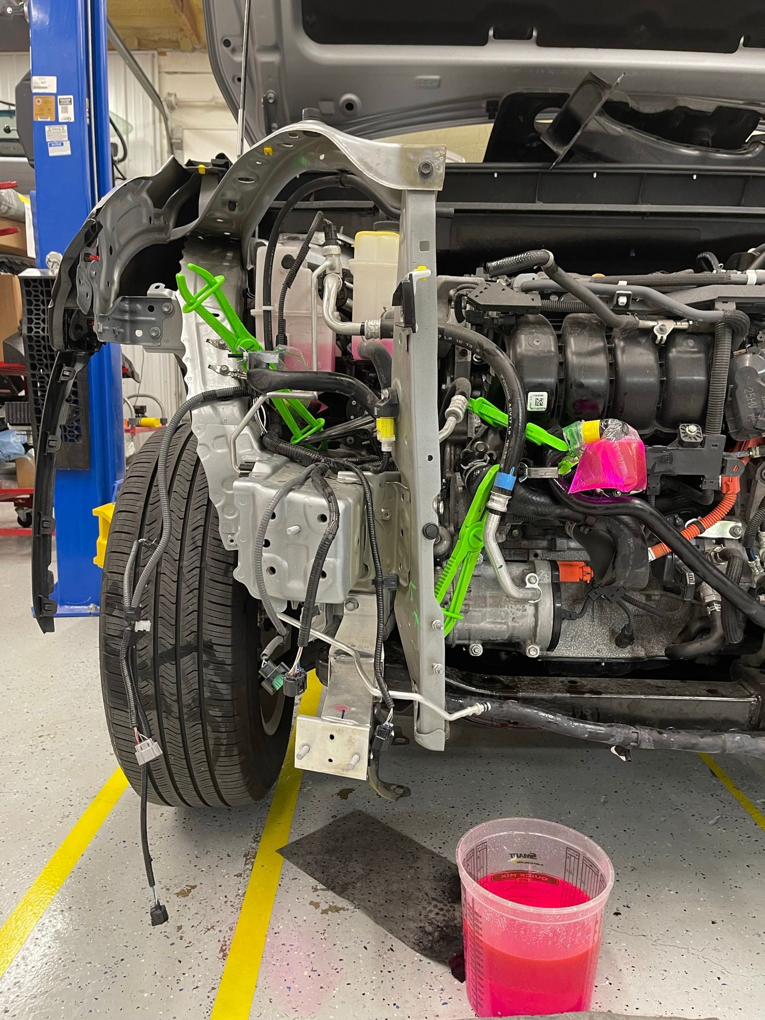 A car is being worked on in a garage with a cup of liquid next to it.