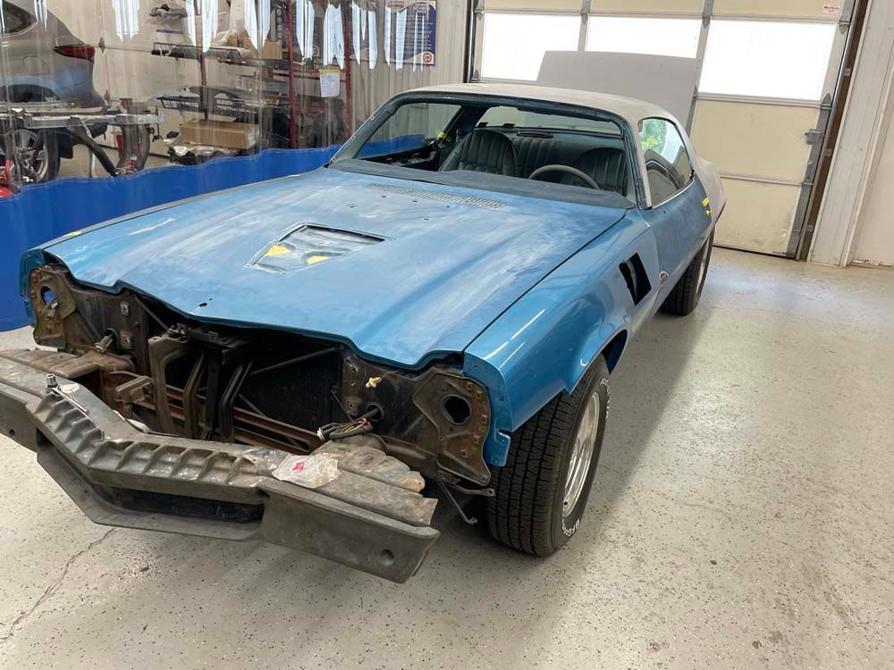 A blue car is sitting in a garage without a hood.