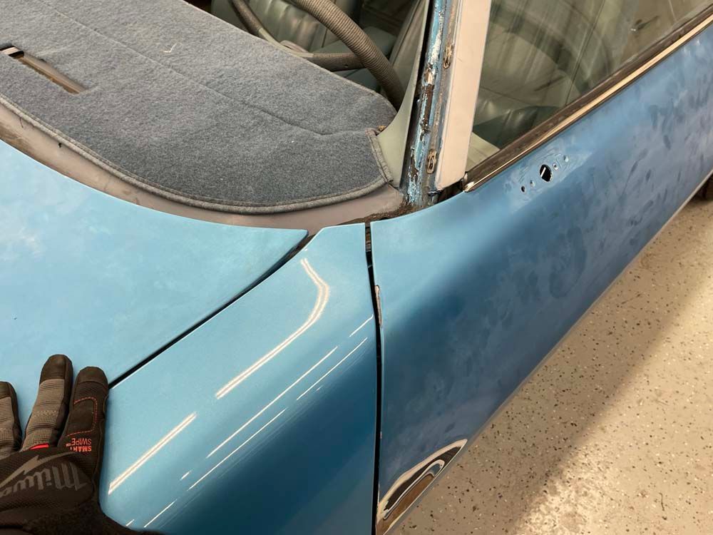 A person wearing black gloves is standing next to a blue car