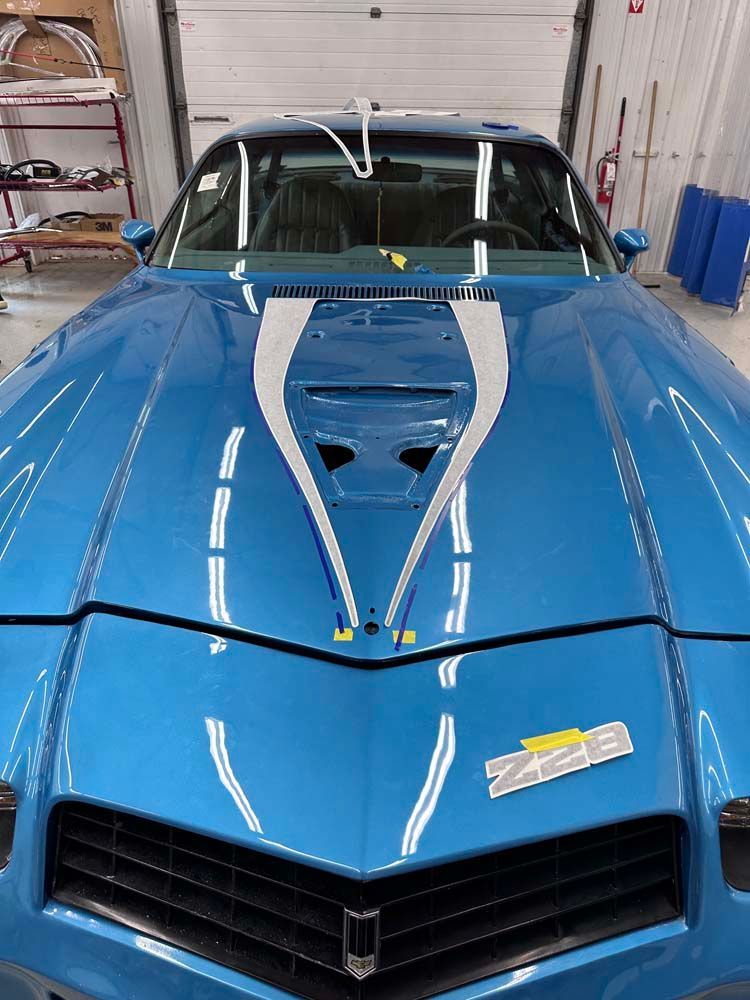 A blue car with a white stripe on the hood is parked in a garage.