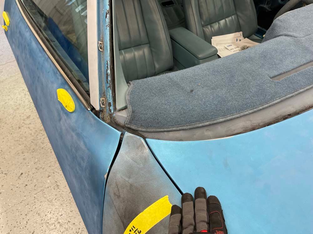 A person is holding a pair of gloves in front of a blue car.