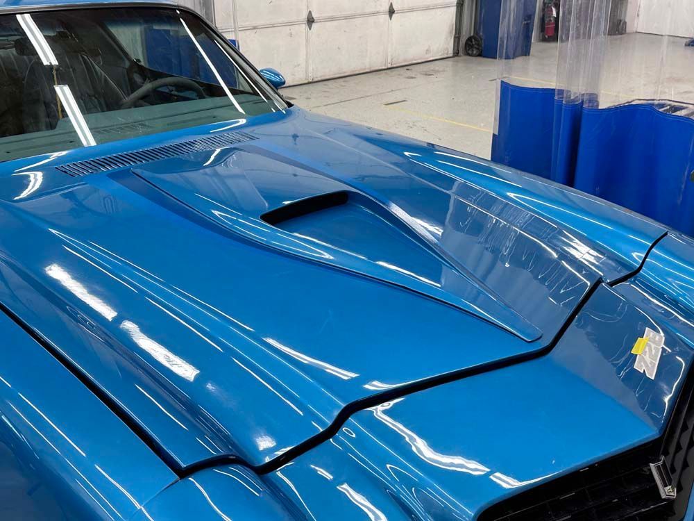 A blue car with the hood open is parked in a garage