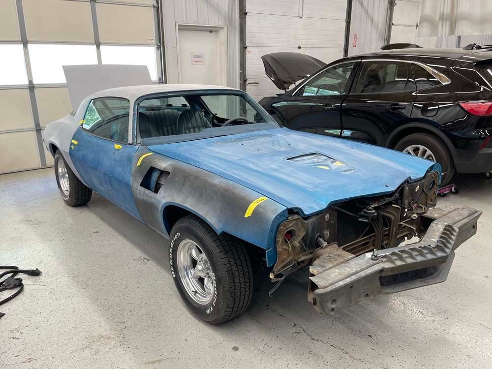 A blue car with the hood up is sitting in a garage next to a black car.