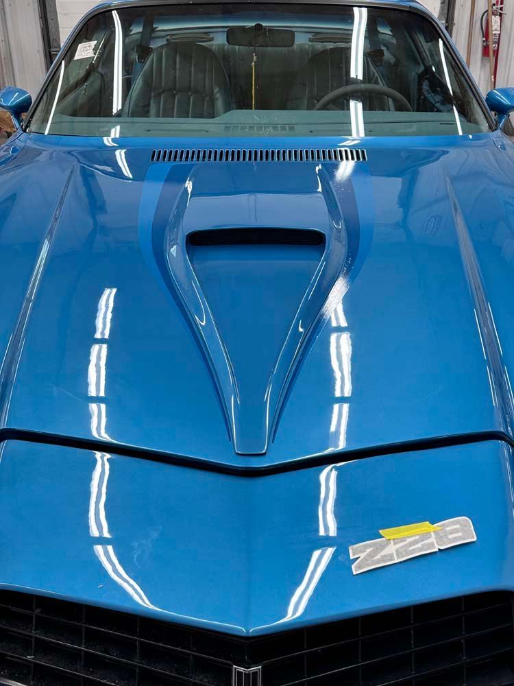 A blue car with a hood that has the letter m on it
