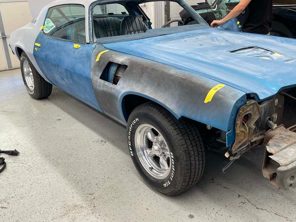 A man is working on a blue car in a garage.