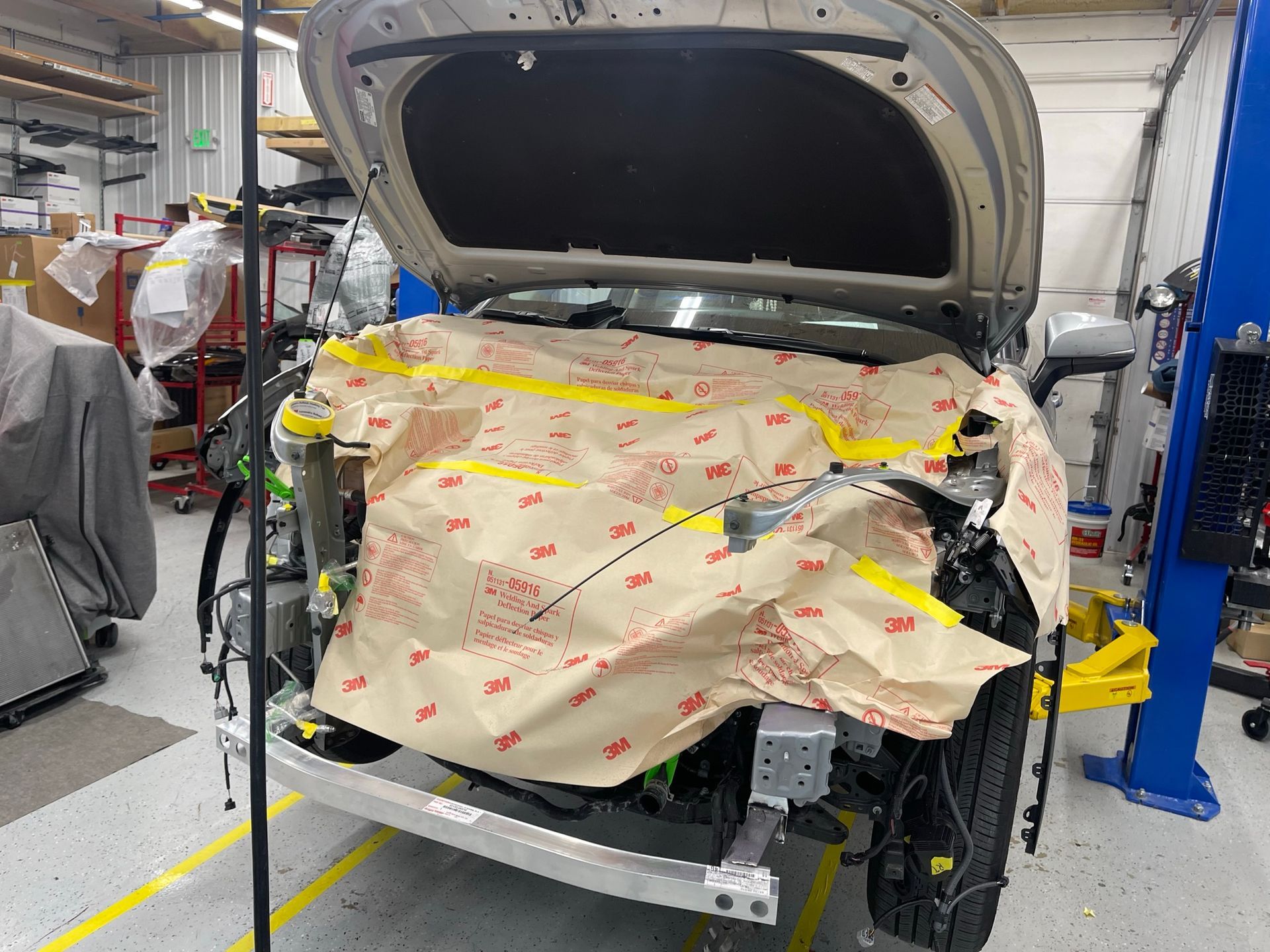 A car is being worked on in a garage with the hood open.