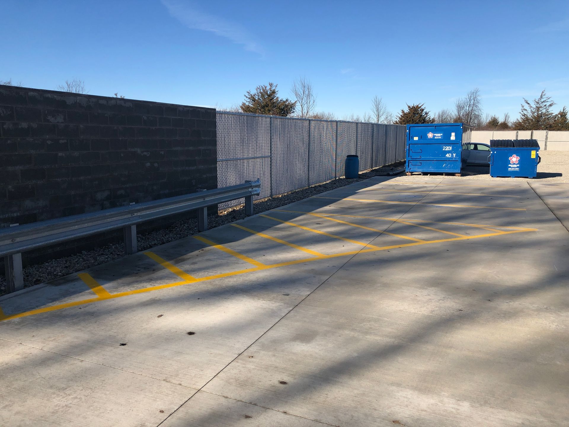 A parking lot with a blue dumpster and a fence