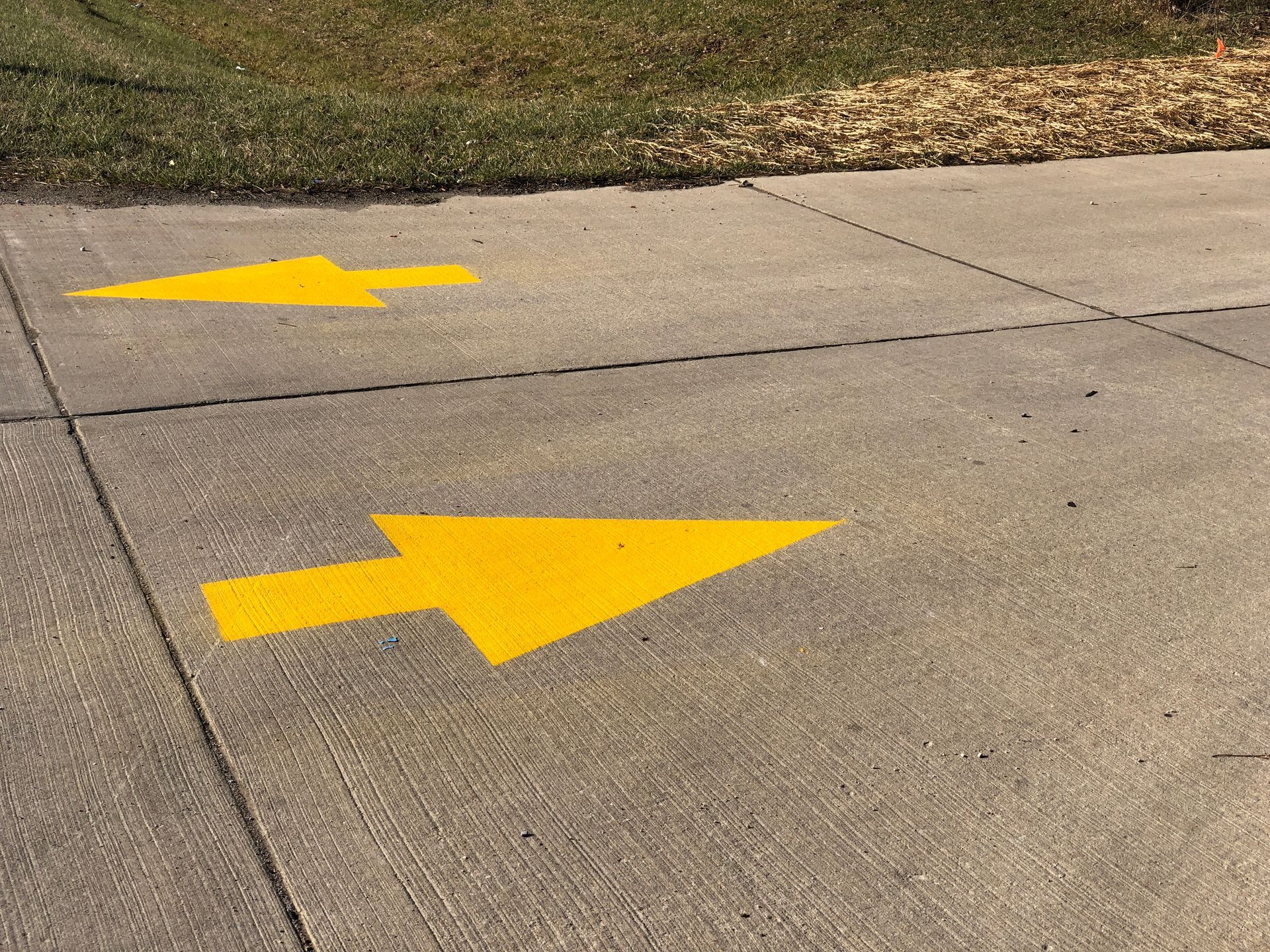 Two yellow arrows painted on the sidewalk pointing in opposite directions.