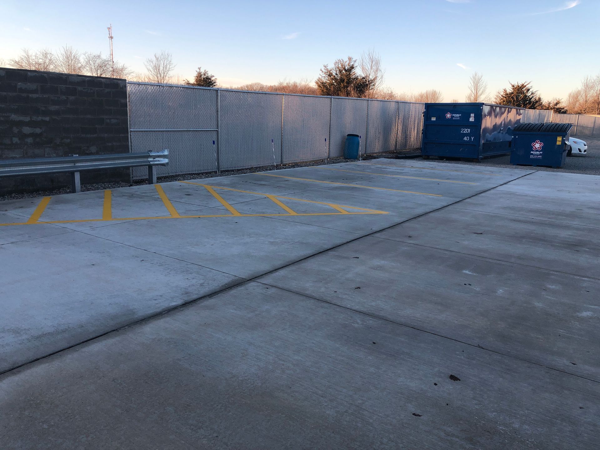 A parking lot with a blue dumpster and a bench