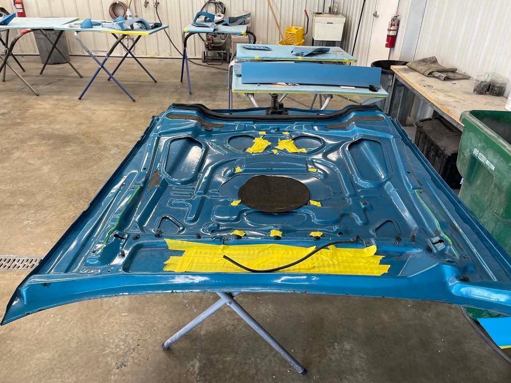 A blue car hood is sitting on a table in a garage.