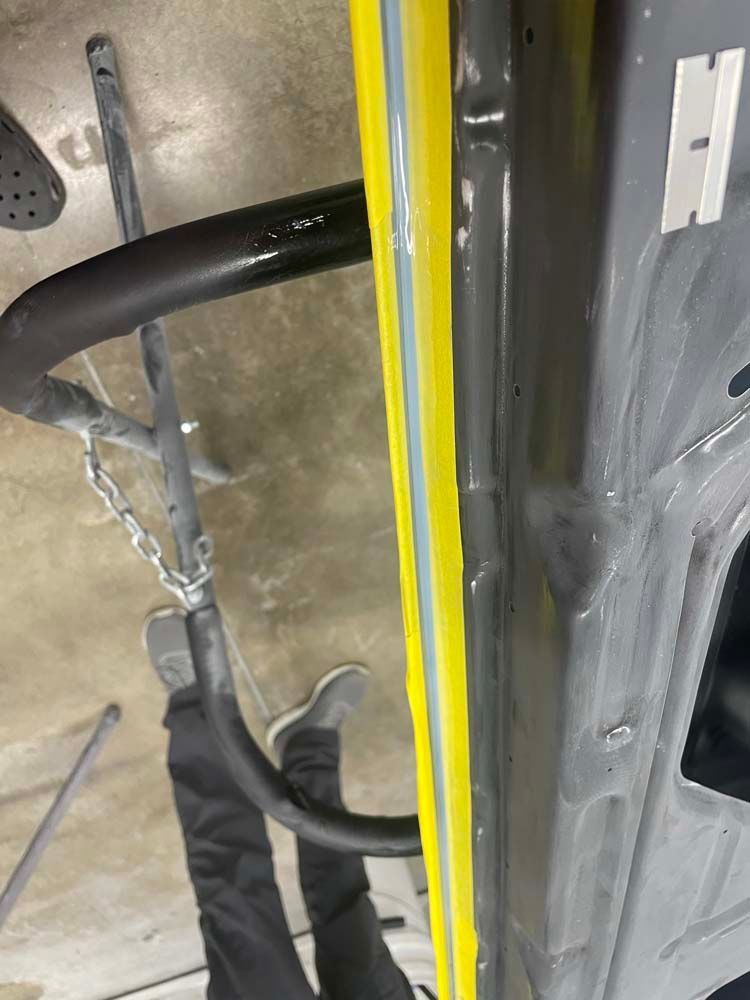 A person is standing next to a gray vehicle with a yellow stripe on the side.