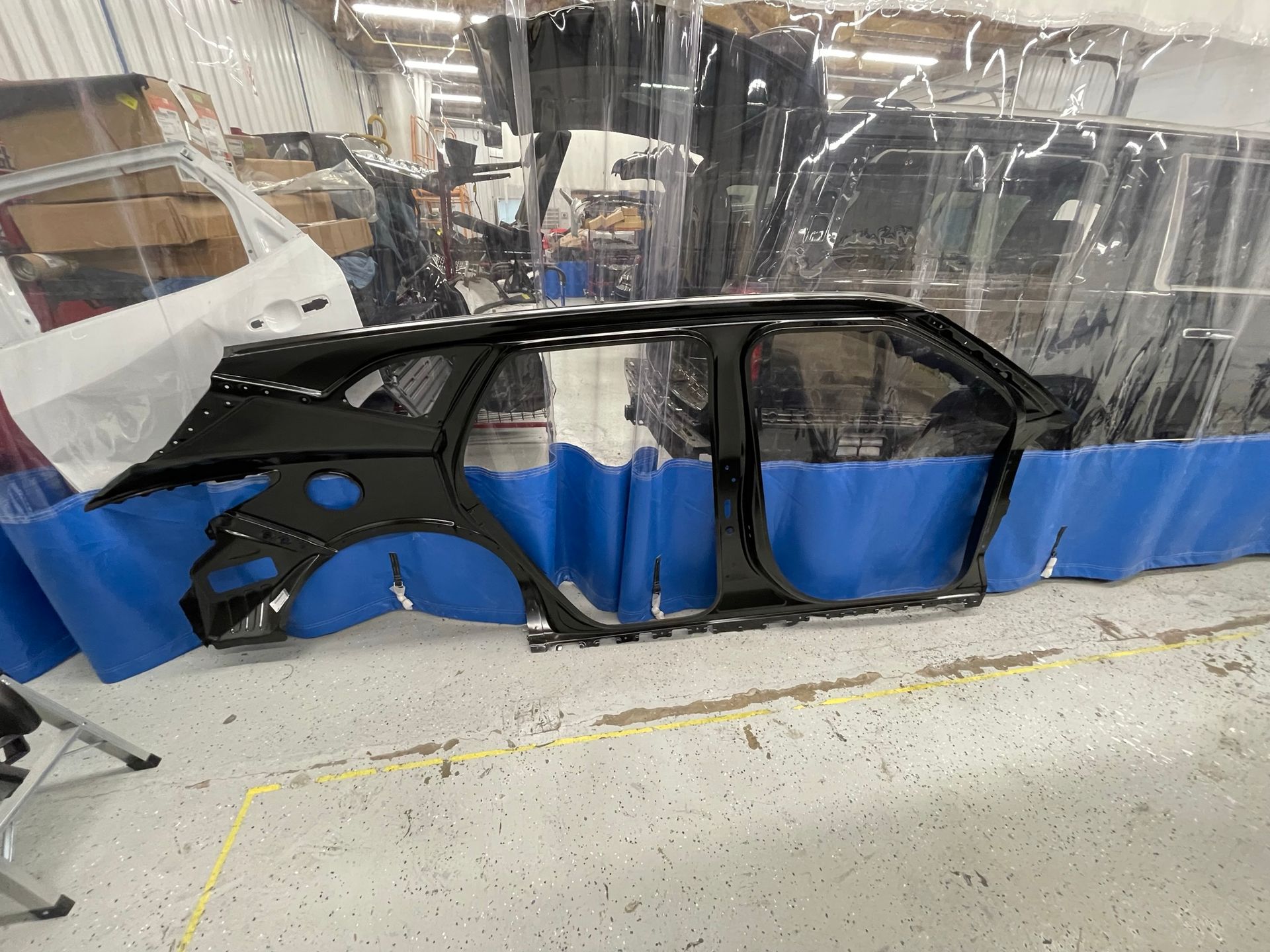 A car is being built in a factory with a blue tarp covering it.