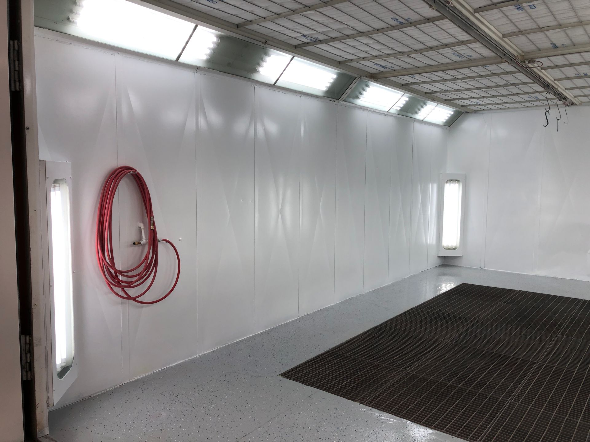 An empty paint booth with a red hose hanging on the wall.