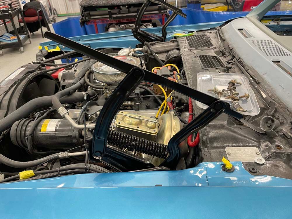 A blue car with the hood open is being worked on in a garage.