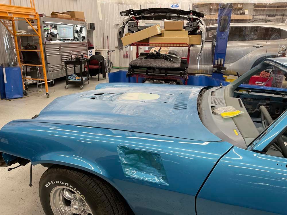 A blue car is parked in a garage with the hood open