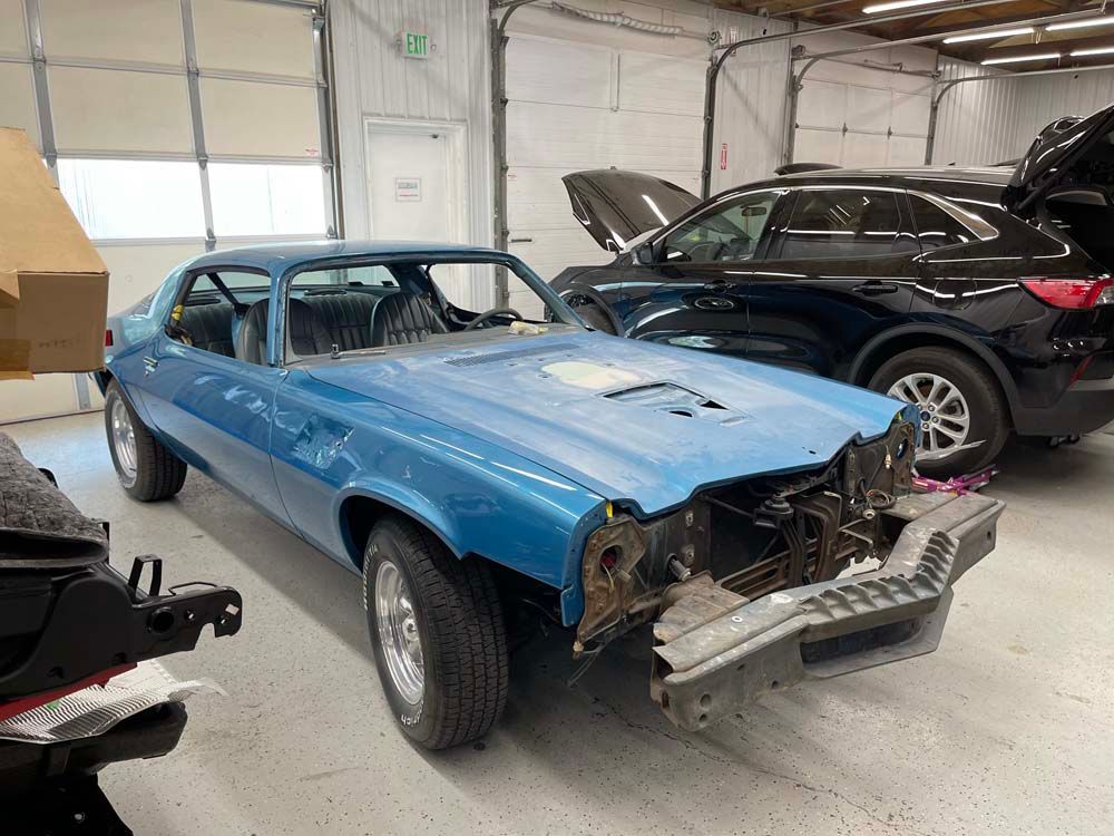 A blue car is sitting in a garage next to a black car.