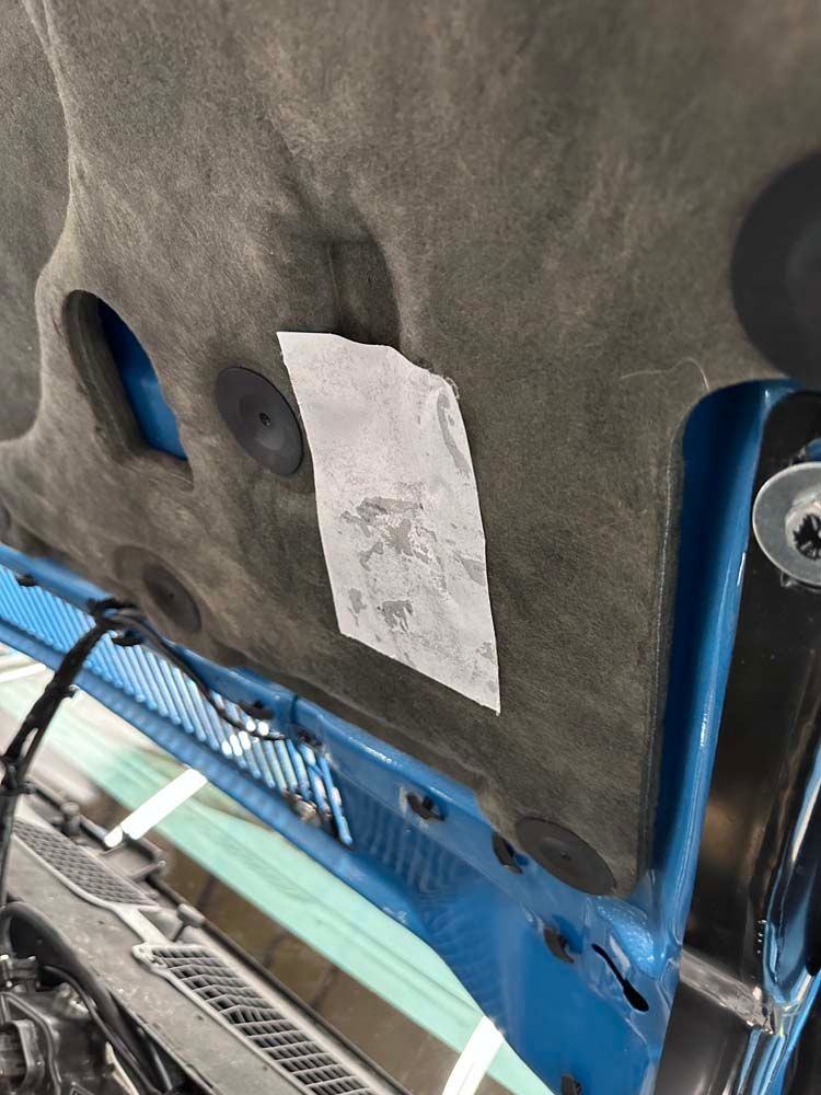 A close up of a blue car hood with a piece of paper on it.
