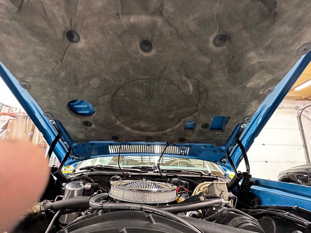A person is looking under the hood of a blue car.