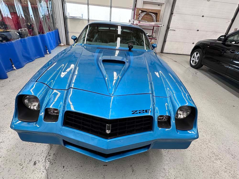 A blue car is parked in a garage next to a black car.