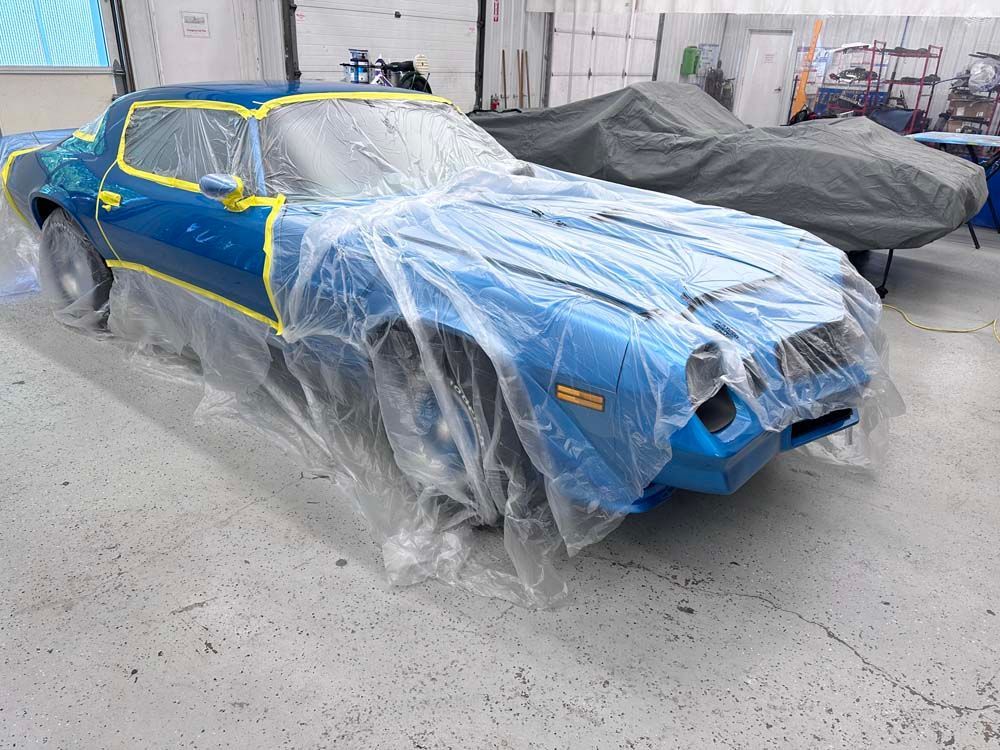 A blue car is wrapped in plastic in a garage.