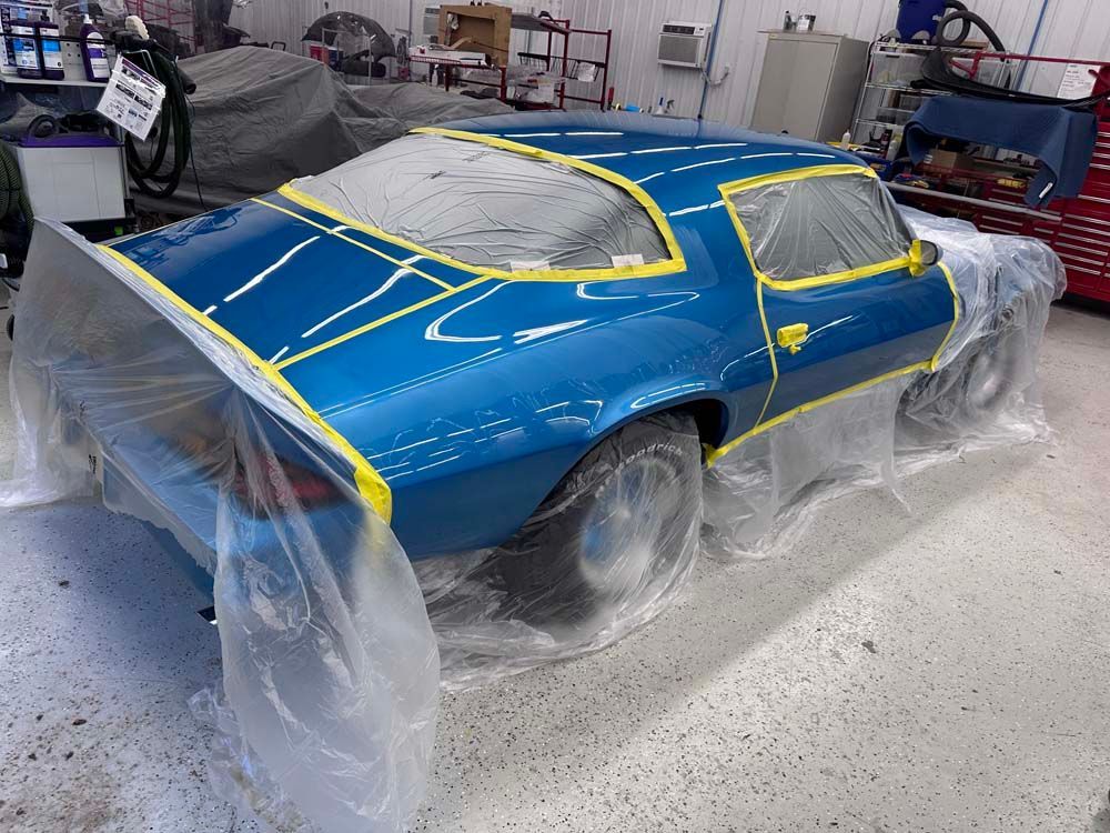 A blue car is wrapped in plastic in a garage.