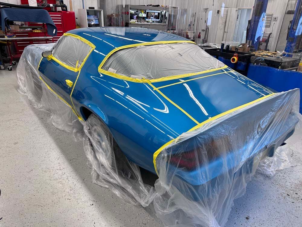 A blue car is wrapped in plastic in a garage