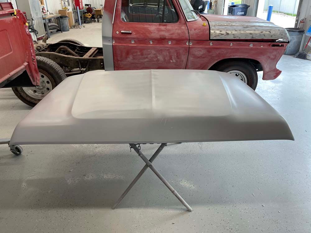 The hood of a red truck is sitting on a table in a garage.