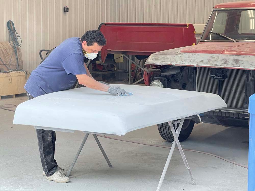 A man wearing a mask is working on a hood of a truck.