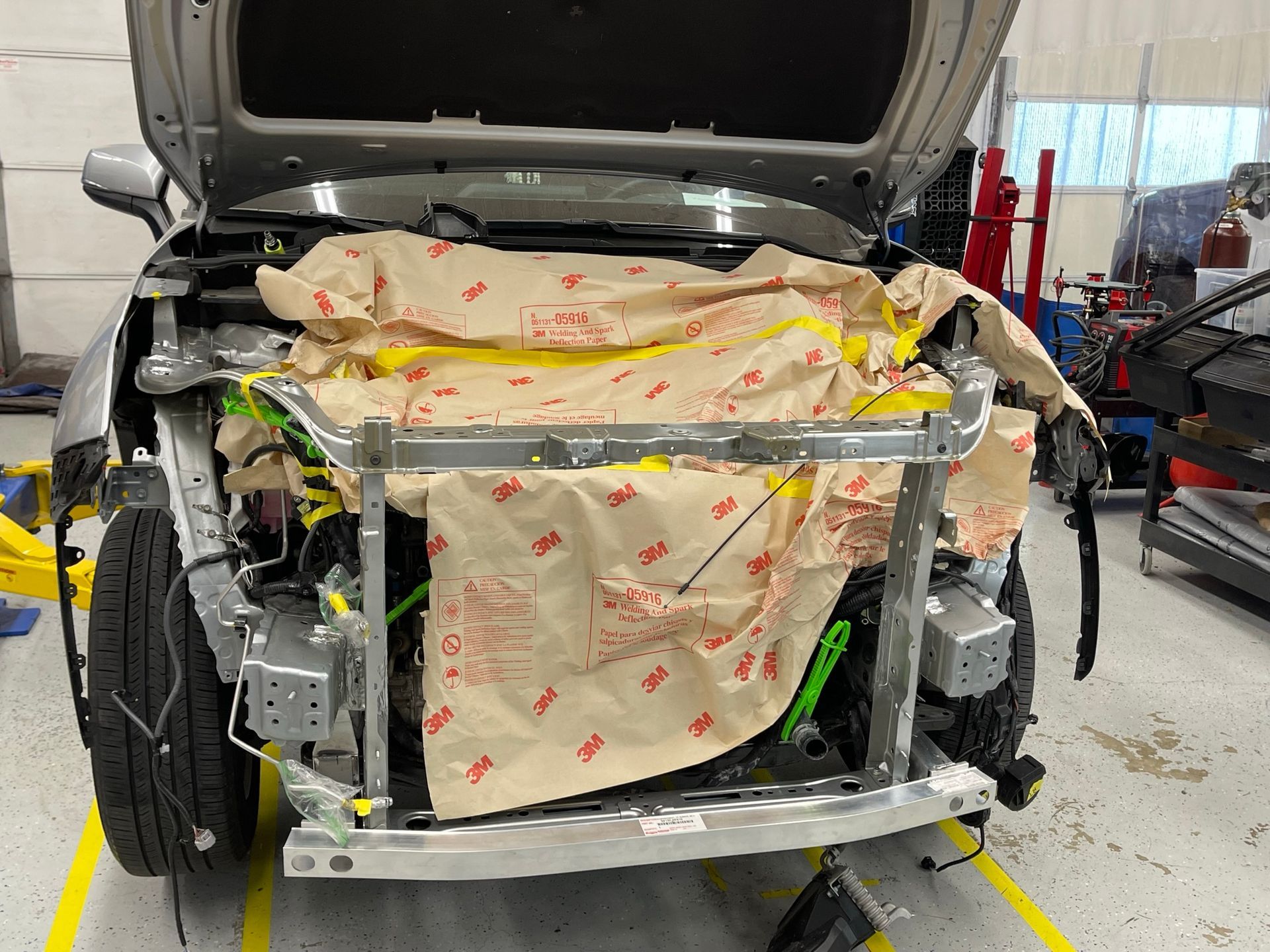 A car is being worked on in a garage with the hood open.