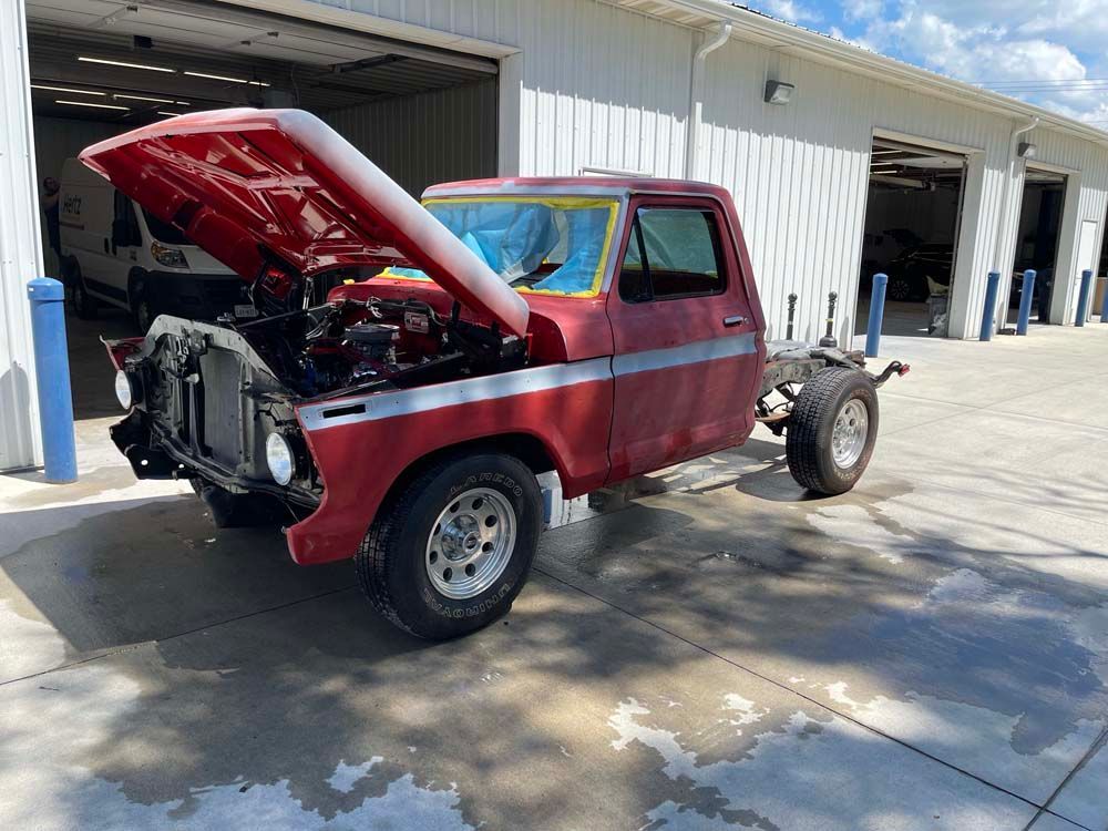 A red truck with the hood up is parked in front of a garage.